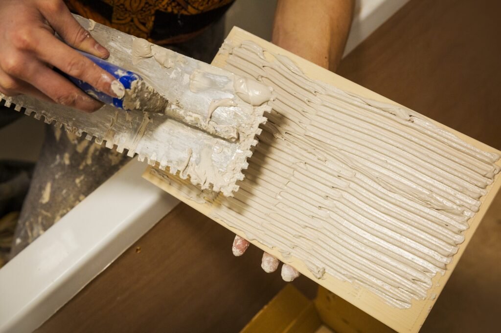 a tiler sitting in a bathtub spreading adhesive on a tile.