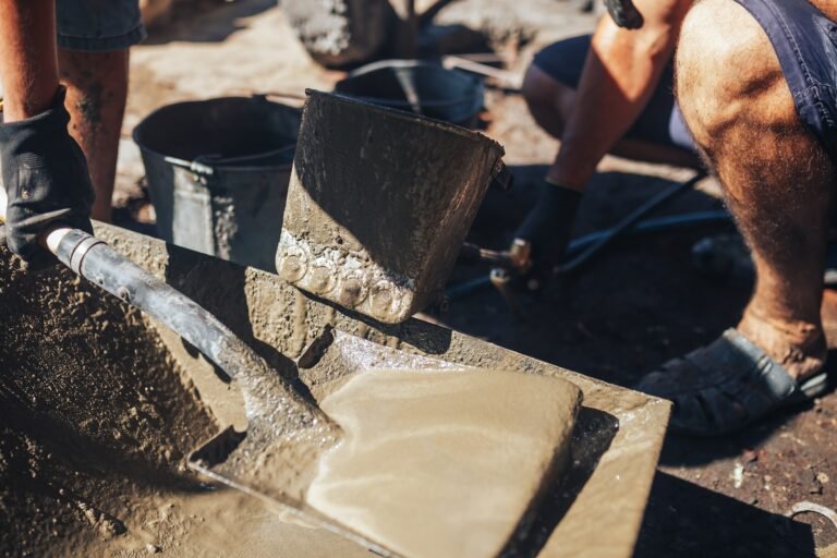 Workers work with cement mortar, loading the hopper bucket with mortar with a shovel