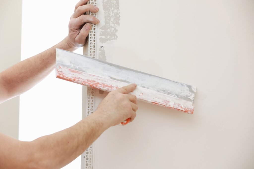 Builder in protective mask plastering wall with putty-knife