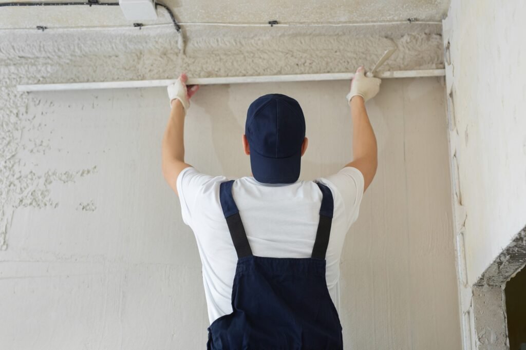 a plasterer holds a metal ruler and aligns a freshly plastered wall
