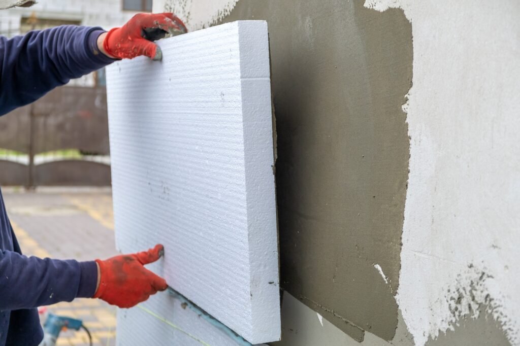 Construction worker installing styrofoam insulation sheets on house facade wall for thermal