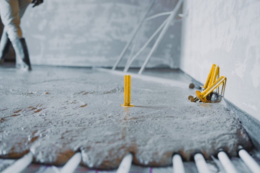 Construction worker pouring concrete surface flooring over underfloor heating system
