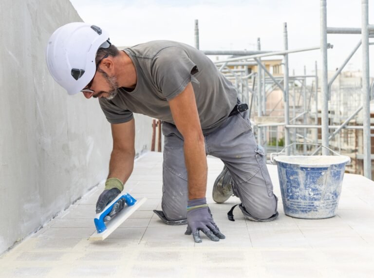 Craftsman in grey work clothes puts grout with a float during construction