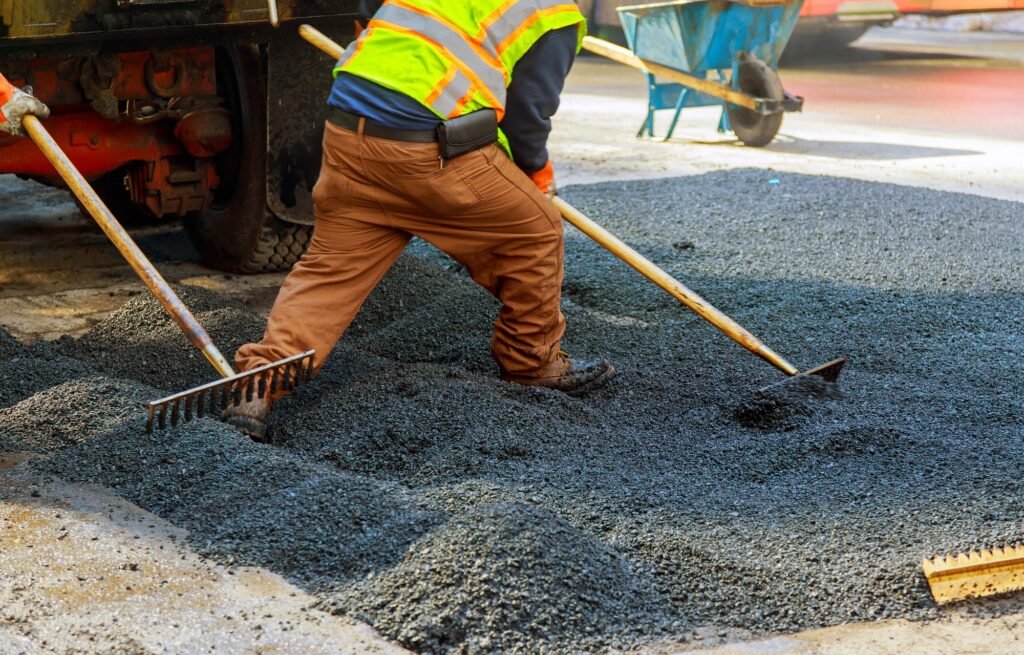 Men at work, urban road under construction, asphalting in progress, workers install sewer manhole