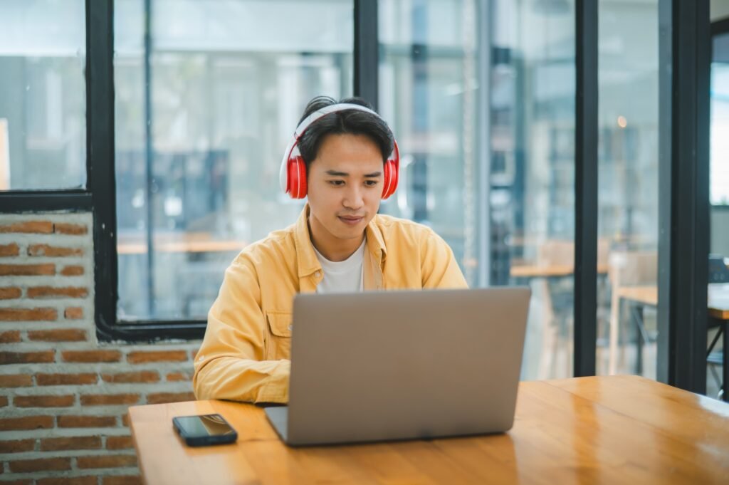 Student using a laptop in a cafe while wearing headphones, learning and searching the internet,